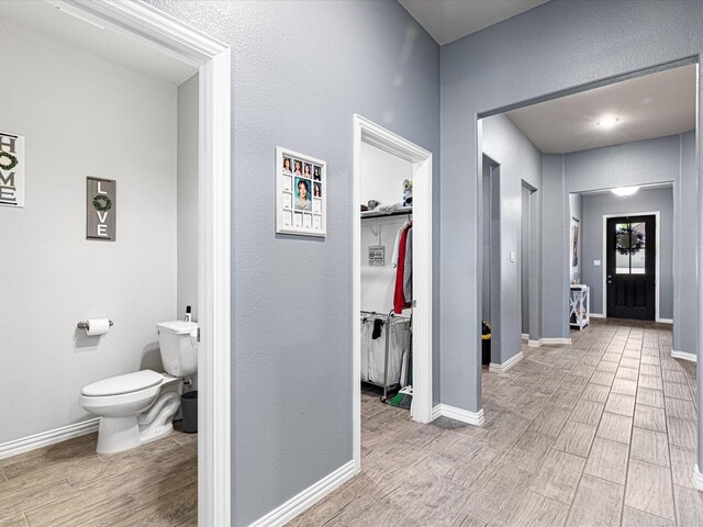 corridor featuring baseboards, a textured wall, and wood finished floors
