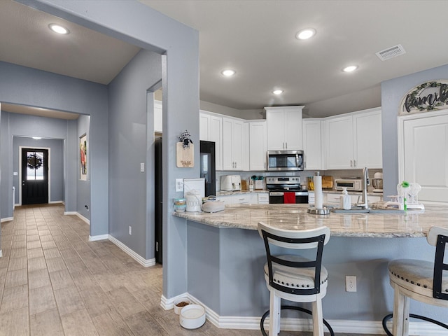 kitchen featuring light stone counters, a breakfast bar, white cabinets, appliances with stainless steel finishes, and visible vents