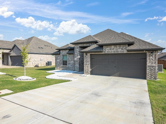 prairie-style home featuring central AC, a front lawn, an attached garage, brick siding, and roof with shingles