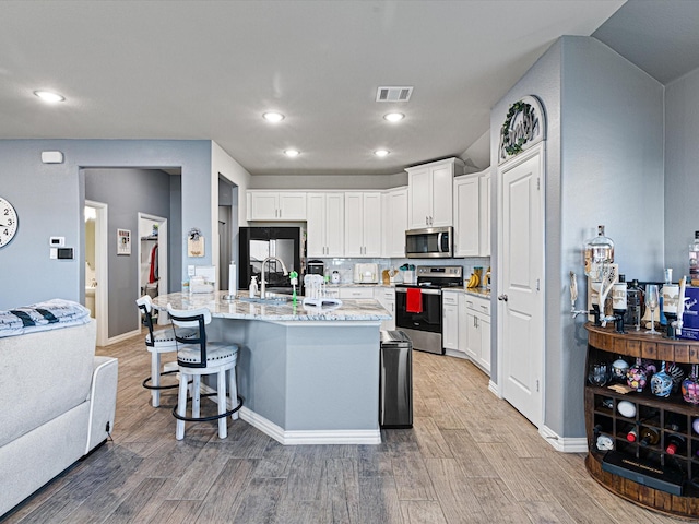 kitchen featuring a breakfast bar area, light wood-type flooring, stainless steel appliances, white cabinets, and visible vents