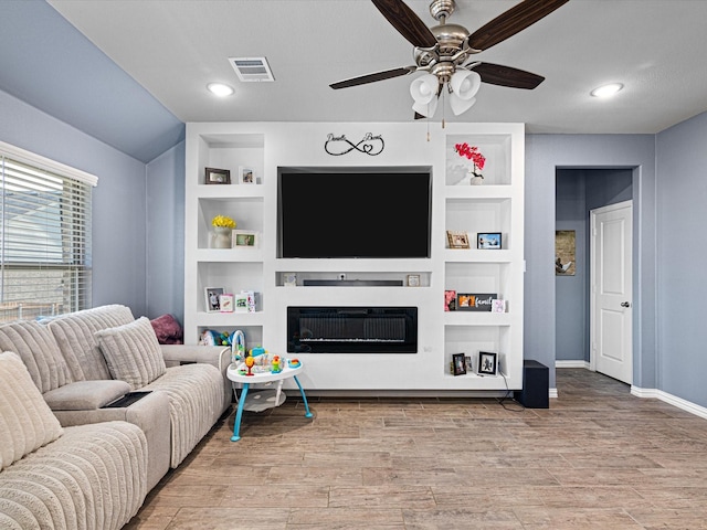 living area featuring built in shelves, light wood-type flooring, visible vents, and a fireplace