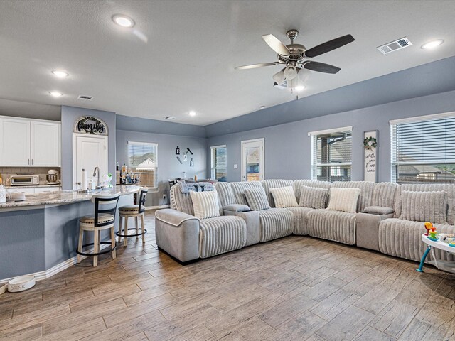 living room with light wood-style flooring, visible vents, a ceiling fan, and plenty of natural light