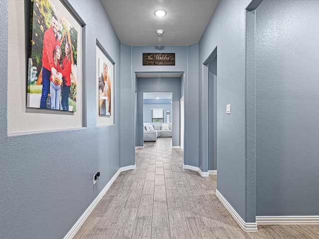 corridor featuring a textured wall, baseboards, wood finished floors, and a textured ceiling