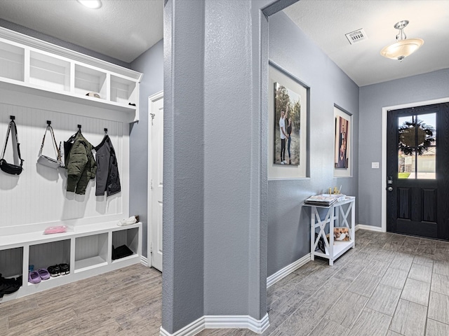 mudroom with visible vents, baseboards, wood finished floors, and a textured wall