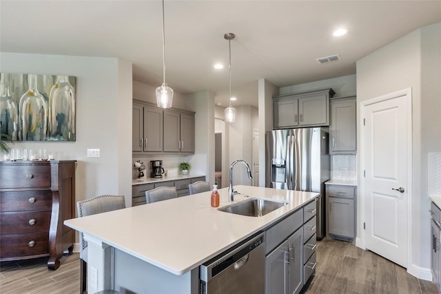 kitchen with wood finished floors, a sink, gray cabinets, appliances with stainless steel finishes, and visible vents