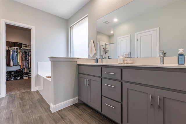 bathroom with a bath, double vanity, visible vents, wood finished floors, and a shower stall