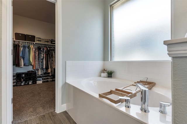 bathroom featuring a walk in closet, wood finished floors, and a garden tub