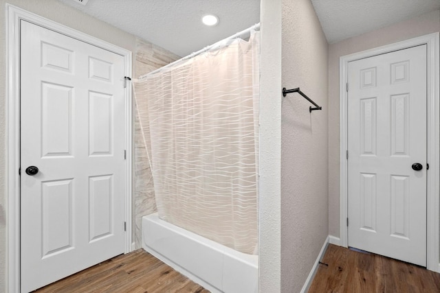 bathroom with shower / bath combination with curtain, a textured wall, wood finished floors, and a textured ceiling