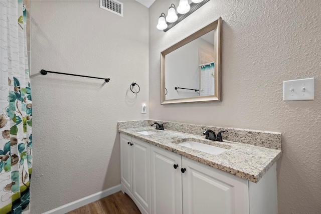 bathroom with wood finished floors, a sink, visible vents, and double vanity