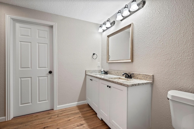 bathroom with toilet, a textured wall, wood finished floors, and a sink