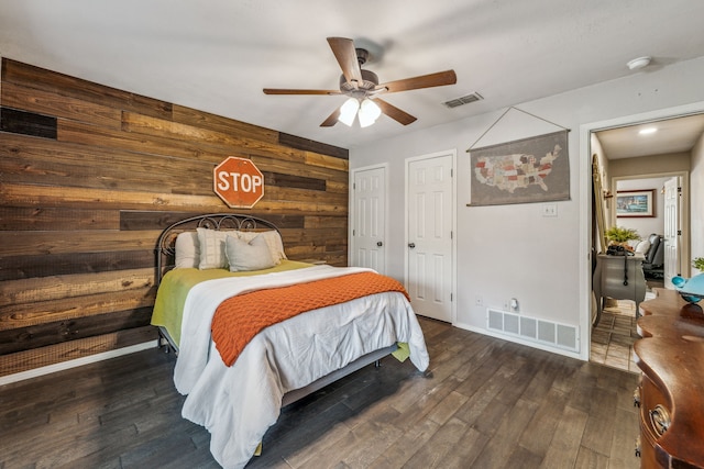 bedroom with wooden walls, a ceiling fan, wood finished floors, and visible vents