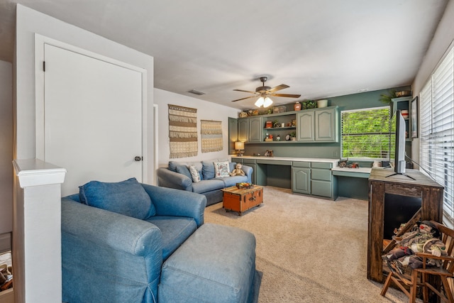 living area featuring light colored carpet, a ceiling fan, visible vents, and built in desk