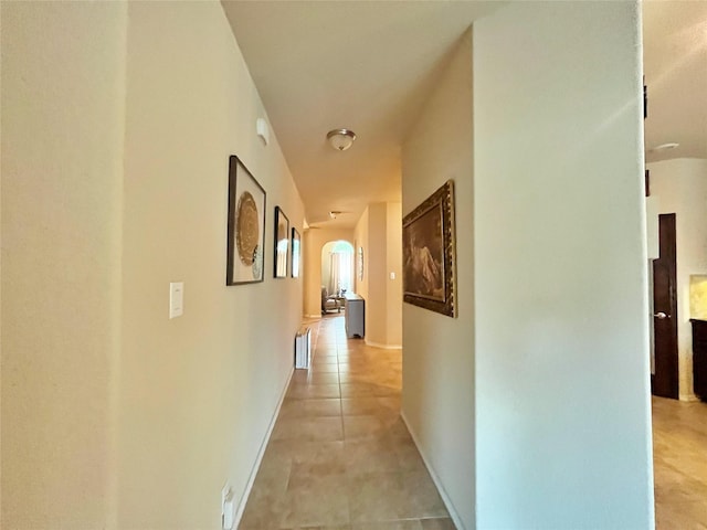 hall with arched walkways and light tile patterned floors