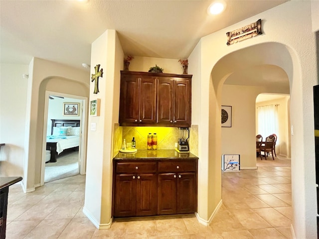 interior space featuring backsplash, dark countertops, dark brown cabinets, light tile patterned floors, and arched walkways