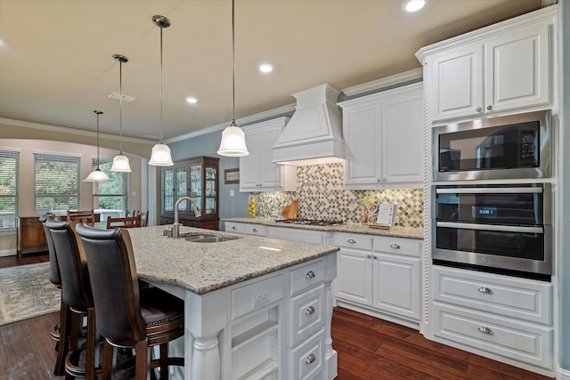 2833 Macquarie St, Trophy Club, TX 76262 - kitchen with custom exhaust hood, an island with sink, a sink, dark wood finished floors, and appliances with stainless steel finishes