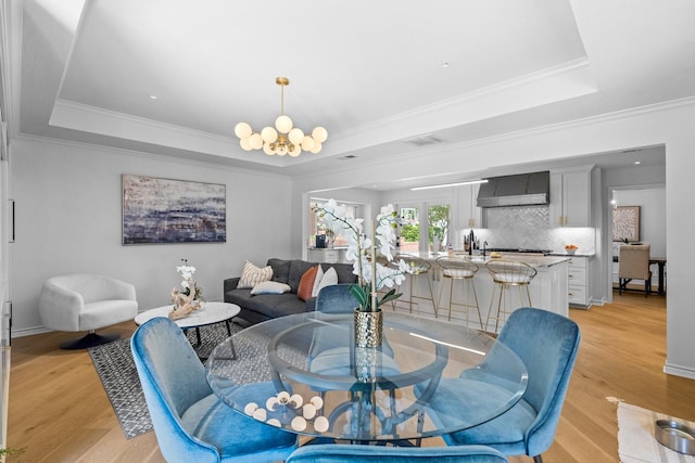 dining area with light wood-style floors, a tray ceiling, and visible vents