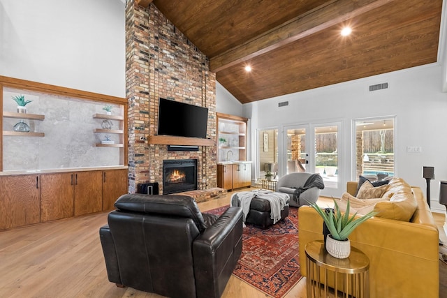 living room with light wood finished floors, a brick fireplace, high vaulted ceiling, wooden ceiling, and beamed ceiling