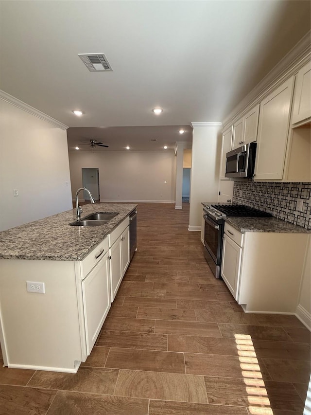 kitchen featuring a sink, an island with sink, stainless steel appliances, ornamental molding, and visible vents