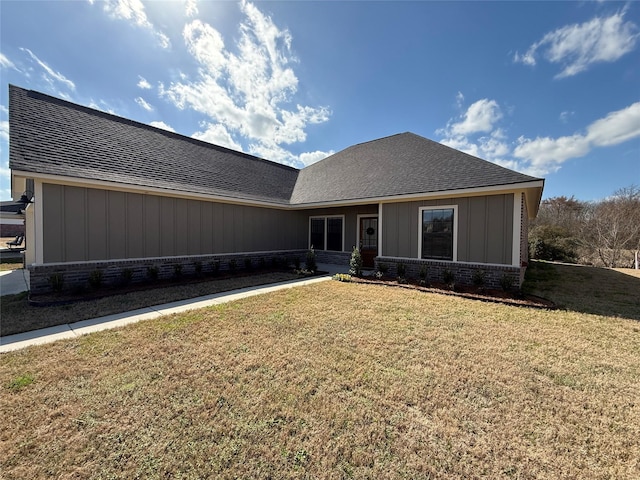 view of front of property with board and batten siding, roof with shingles, a front yard, and brick siding
