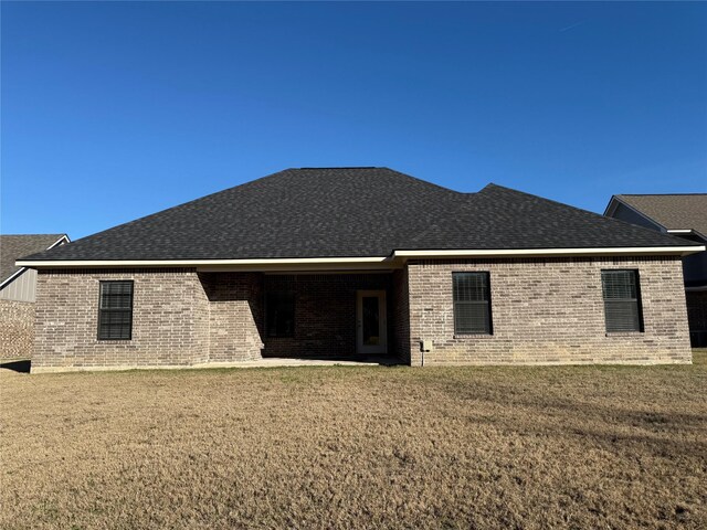 rear view of property with a lawn, brick siding, and roof with shingles