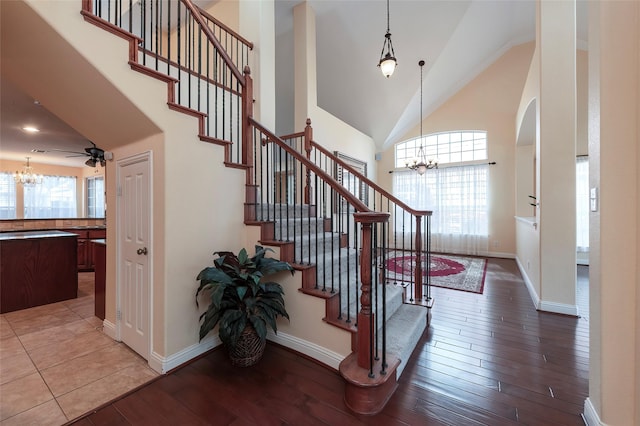 staircase with high vaulted ceiling, baseboards, a notable chandelier, and wood finished floors