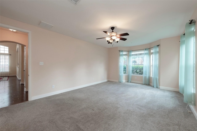 unfurnished room featuring arched walkways, plenty of natural light, baseboards, and ceiling fan