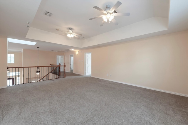 empty room with a ceiling fan, a tray ceiling, baseboards, carpet flooring, and visible vents