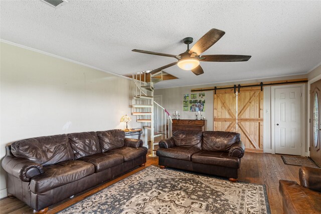 living area with ceiling fan, a textured ceiling, crown molding, a barn door, and wood-type flooring