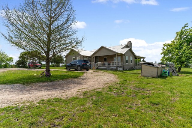 view of front of property featuring dirt driveway, a chimney, a front lawn, and covered porch