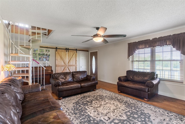 living room featuring ceiling fan, a barn door, a textured ceiling, stairs, and baseboards