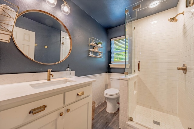 bathroom featuring toilet, wainscoting, wood finished floors, a shower stall, and vanity