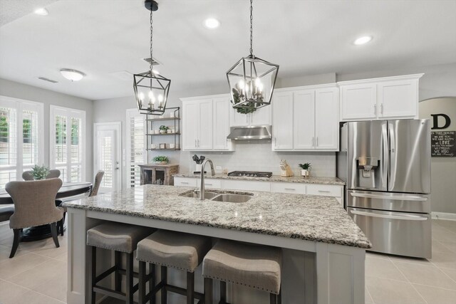 kitchen with white cabinetry, under cabinet range hood, a sink, light tile patterned floors, and stainless steel appliances