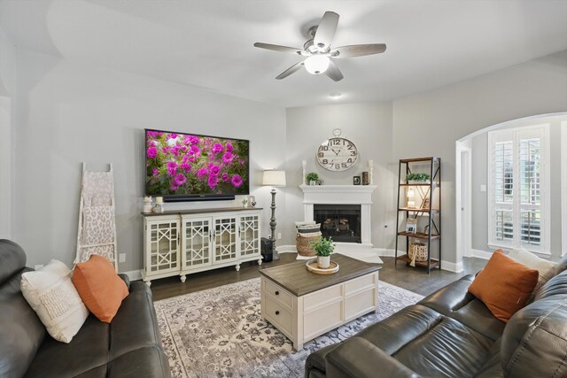 living room with wood finished floors, baseboards, a fireplace with raised hearth, arched walkways, and a ceiling fan