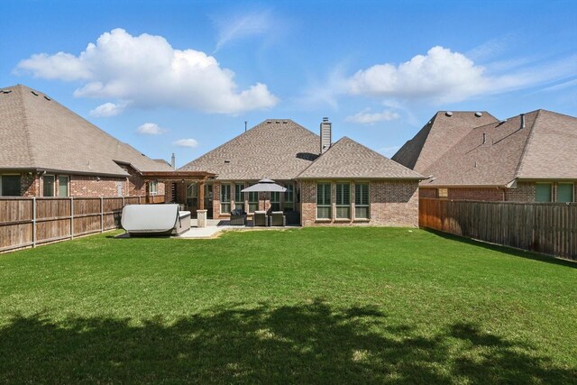 back of property with a fenced backyard, a chimney, brick siding, a patio area, and a yard