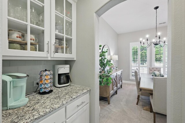 kitchen with glass insert cabinets, light carpet, white cabinetry, and a notable chandelier