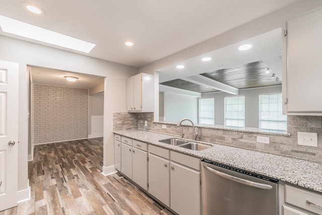 kitchen featuring stainless steel dishwasher, a sink, light wood-style floors, a skylight, and decorative backsplash