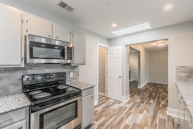 kitchen featuring a skylight, decorative backsplash, light wood-type flooring, appliances with stainless steel finishes, and visible vents