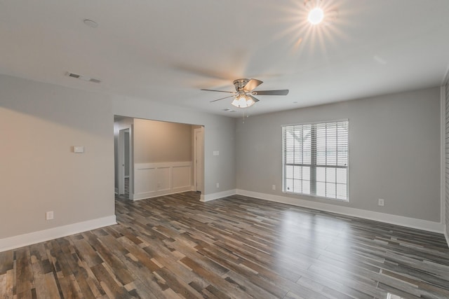 spare room featuring baseboards, a ceiling fan, visible vents, and dark wood finished floors