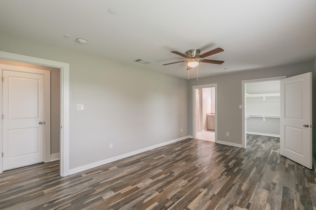 unfurnished bedroom with a closet, a spacious closet, baseboards, dark wood-type flooring, and visible vents