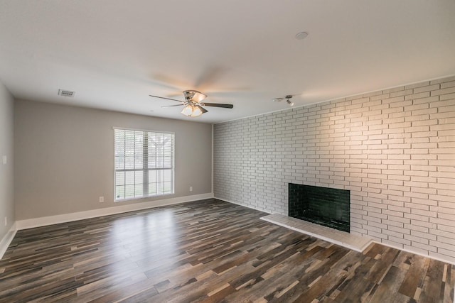 unfurnished living room featuring visible vents, brick wall, ceiling fan, a fireplace, and dark wood-type flooring