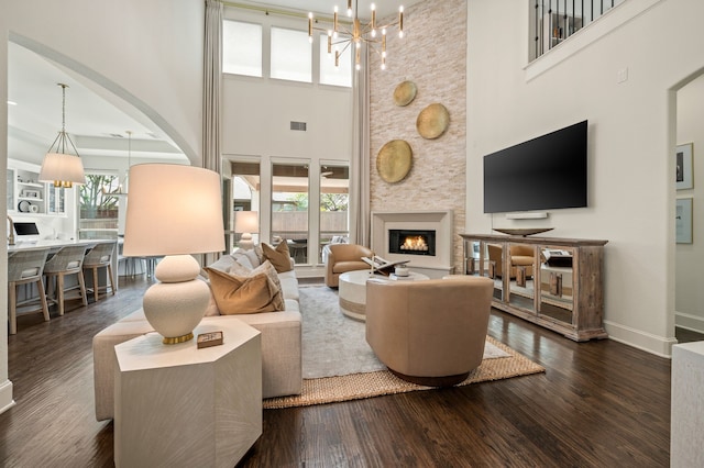 living room featuring a chandelier, a towering ceiling, dark wood-style floors, and a fireplace