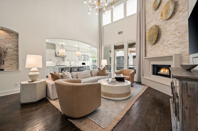 living room featuring a lit fireplace, a towering ceiling, and dark wood-type flooring