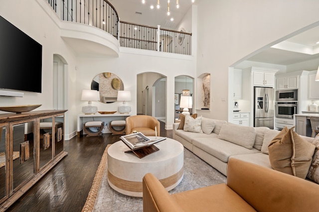 living room featuring baseboards, a high ceiling, arched walkways, and dark wood finished floors