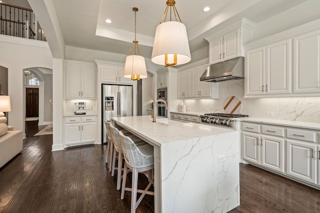 kitchen featuring recessed lighting, under cabinet range hood, stainless steel appliances, arched walkways, and decorative backsplash