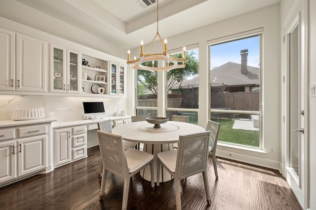 dining space featuring built in study area, dark wood finished floors, a chandelier, and visible vents
