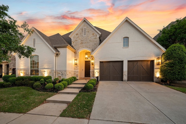 french country style house featuring stone siding, a front lawn, a garage, and concrete driveway