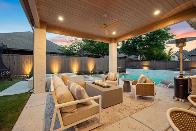 patio terrace at dusk featuring a ceiling fan, a fenced backyard, a fenced in pool, and an outdoor living space with a fire pit