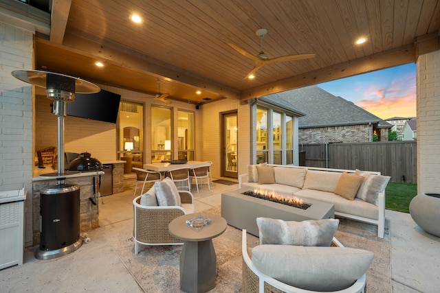 patio terrace at dusk with fence, ceiling fan, outdoor dining area, and an outdoor living space with a fire pit