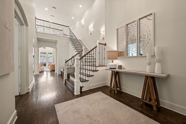 foyer entrance with stairway, arched walkways, wood finished floors, and a high ceiling