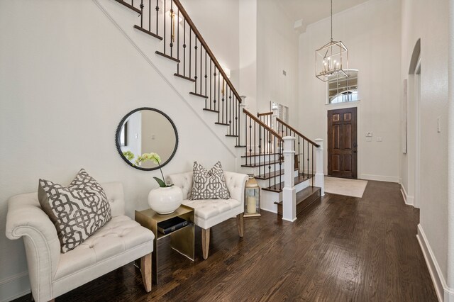 foyer featuring dark wood-style floors, a towering ceiling, baseboards, an inviting chandelier, and stairs